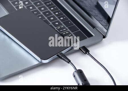 Connect smartphone to laptop for data dump via USB cable on white table. Stock Photo