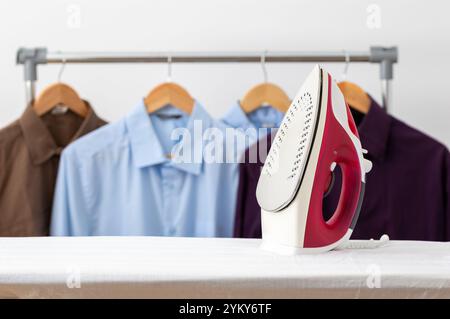 Electric iron and pile of clothes on ironing board at home with copy space. Stock Photo