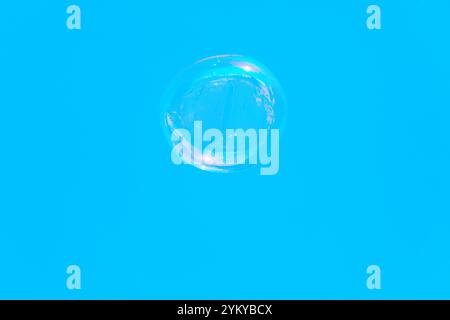 Single transparent bubble floating against a bright blue background. Bubble is spherical and appears to have some reflections and slight distortions o Stock Photo
