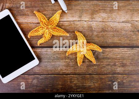 Starfish are arranged next to digital tablet PC on rustic wooden table with purchase online vacation ticket Stock Photo