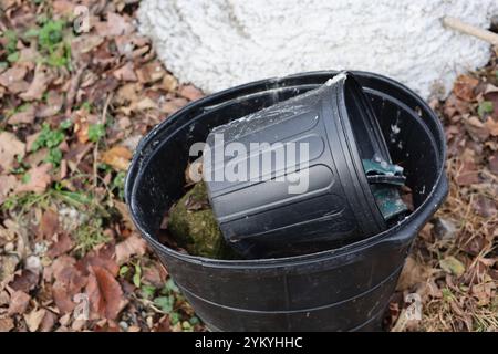 Old black plastic flowerpots outside with fall leaves on ground Stock Photo