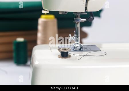 Sewing machine with black thread and spools on table in crafting space during daylight Stock Photo