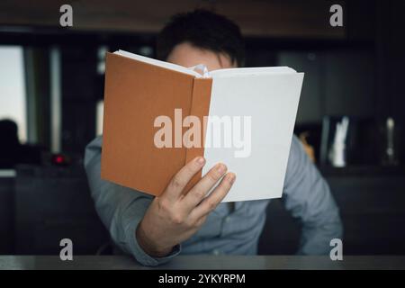 man reading book on couch. Bearded male thoughtfully studying literature. Stock Photo