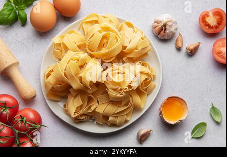 Plate of raw, uncooked pappardelle pasta surrounded by fresh ingredients, ready for cooking Stock Photo