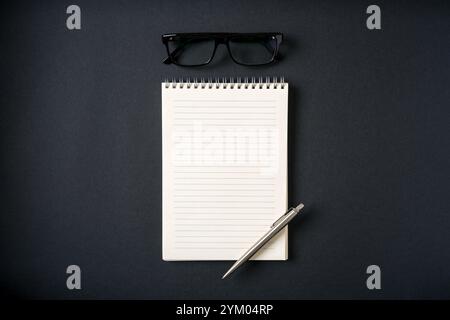 Top view of notebook, glasses and ballpoint pen on dark grey background Stock Photo