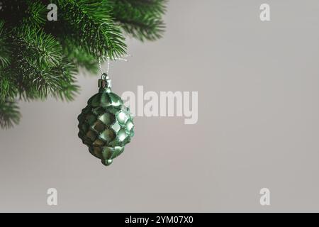 Christmas tree toy in the shape of a green pine cone hanging from a christmas tree branch on grey background representing christmas and new year, with Stock Photo