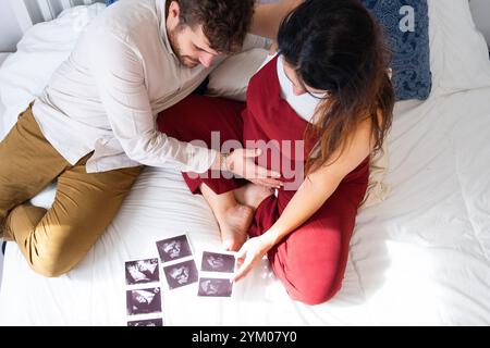 Couple with pregnant woman looking at ultrasound photos of the baby in bed at home Stock Photo