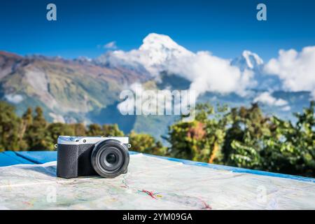Compact digital camera placed on a map in front of beautifaul snow-covered peak of mountain, Annapurna, Nepal Stock Photo
