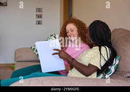 Two female students studying together on sofa at home Stock Photo