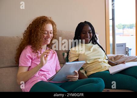 Two female students collaborating, studying together on sofa at home Stock Photo