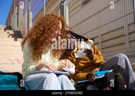 Cheerful students eating sandwiches and having fun on university steps Stock Photo
