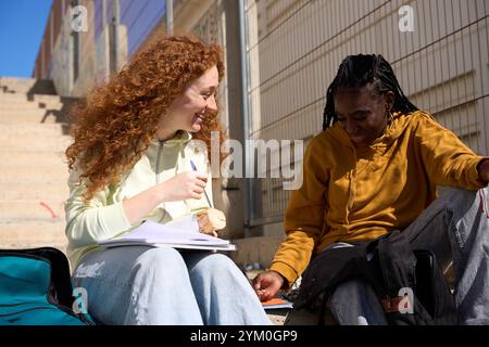 Two smiling students studying and eating together outdoors Stock Photo