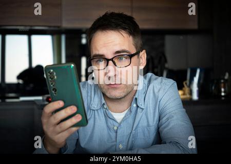 male use modern cellphone gadget, texting or messaging on wireless internet. Caucasian man in glasses sit at desk at home office look at smartphone sc Stock Photo