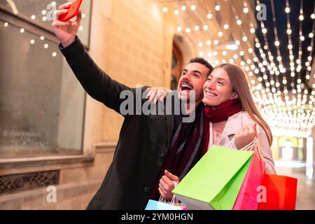 Couple taking a selfie while shopping under festive holiday lights at night Stock Photo