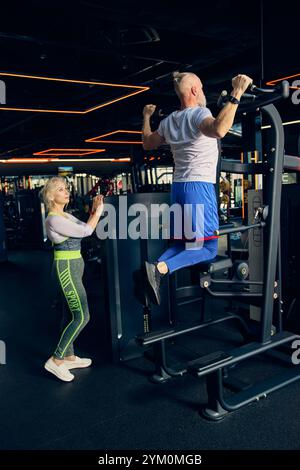 Senior sportive man in sportswear training in gym, doing pull-up exercises in modern gym with special equipment. Stock Photo