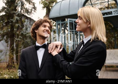 In a vibrant outdoor location, a young couple in elegant black suits share a joyful moment. Their expressions reflect happiness and affection, surroun Stock Photo