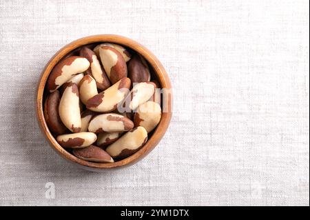 Brazil nuts in wooden bowl on linen fabric, with empty space for text. Shelled, dried seeds of Bertholletia excelsa. Stock Photo