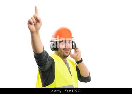 Cheerful adult constructor man wearing orange safety helmet and fluorescent vest at work dancing while listening to music in headphones isolated on wh Stock Photo
