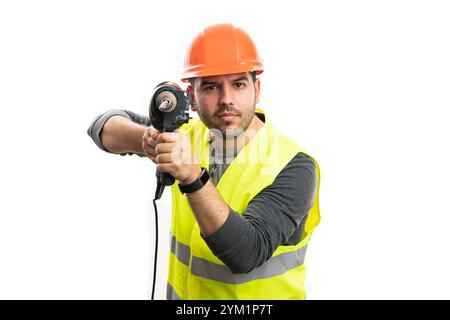 Serious male builder wearing yellow fluorescent vest and safety hardhat pointing electric drilling power tool at camera isolated on white background Stock Photo