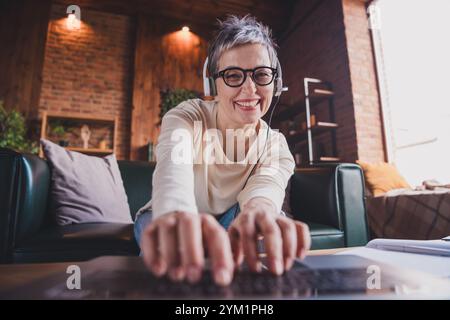 Happy elderly woman with short grey hair in casual style, enjoying leisure time indoors, typing on laptop with a cheerful smile Stock Photo