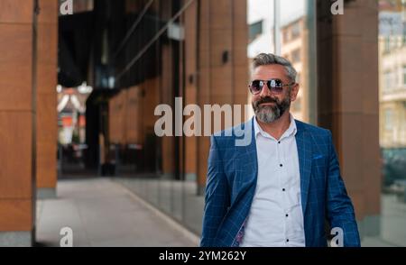A handsome mature business man is walking through the city street near the office building. Stock Photo