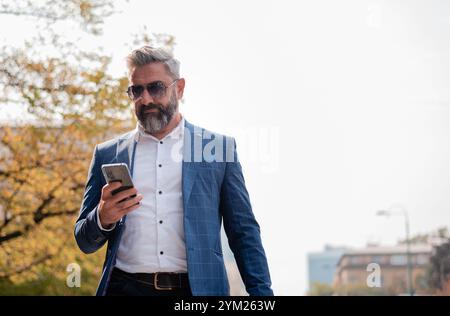 A handsome mature business man using mobile phone app texting in the city street. Stock Photo