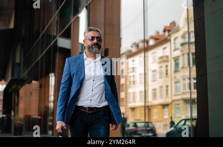 A handsome mature business man is walking through the city street near the office building. Stock Photo