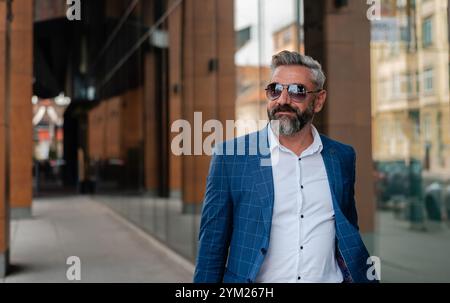 A handsome mature business man is walking through the city street near the office building. Stock Photo