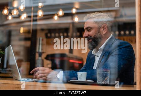 A happy mature business man using his laptop at a restaurant cafe. Stock Photo