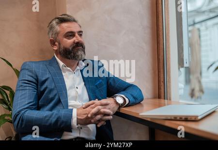 Portrait of a successful mature business man sitting at his desk in the office or restaurant cafe near the window and relaxing after he was works on a Stock Photo