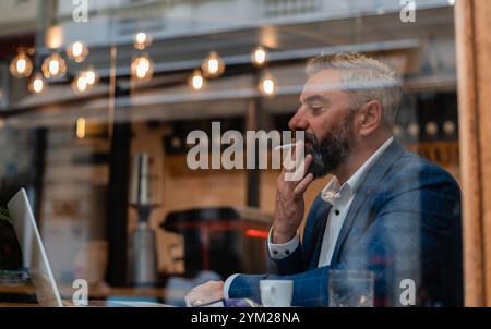 A handsome mature business man using his laptop at a restaurant cafe drinking coffee and smoking a cigarette. Stock Photo