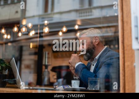 A handsome mature business man using his laptop at a restaurant cafe drinking coffee and smoking a cigarette. Stock Photo
