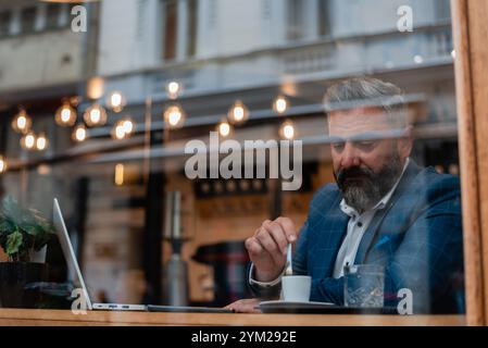 A handsome mature business man drinking a coffee while working on a laptop at a restaurant cafe. Stock Photo