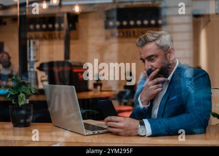 A thoughtful worried mature business man thinking of problem solution while working on a laptop in the office near the window. Stock Photo
