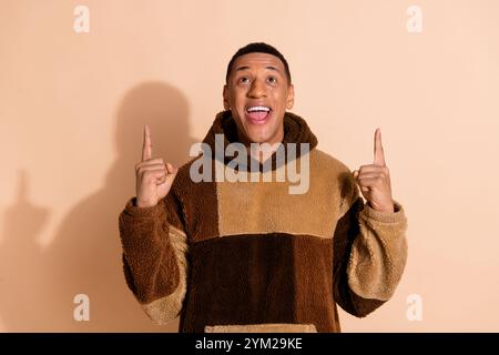 Portrait of overjoyed guy with stylish haircut wear fluffy hoodie look directing at logo empty space isolated on pastel color background Stock Photo