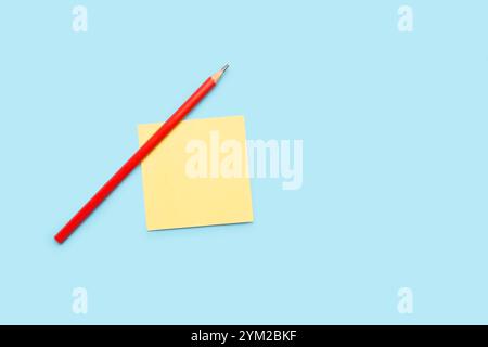 A pencil and a yellow paper note on a light blue background Stock Photo