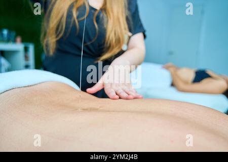 A woman is massaging a man's back with a small stream of water. The man is laying on a bed and the woman is standing behind him. The scene is relaxing Stock Photo