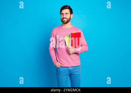 Confident man holding colorful notebooks in casual attire against blue background, symbolizing education and stylish creativity Stock Photo