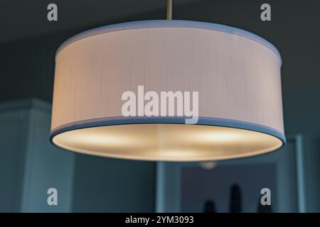 A white lampshade with a blue stripe is lit up. The light is on and the lampshade is glowing Stock Photo