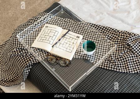A tray with a book, a pen, and a bowl of water on a bed. The tray is on a bed with a blanket and a pillow. The book is a maze puzzle book Stock Photo