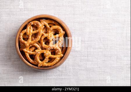 Salted pretzels in a wooden bowl on linen fabric, with empty space for text. Golden toasted small pretzels, in the traditional shape of a loop. Stock Photo