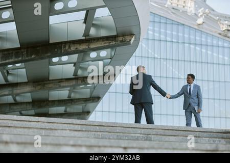 Two Businessmen Shaking Hands on Stairs Outside Modern Office Building With Glass Facade Capturing Professional Interaction and Contemporary Architecture Stock Photo
