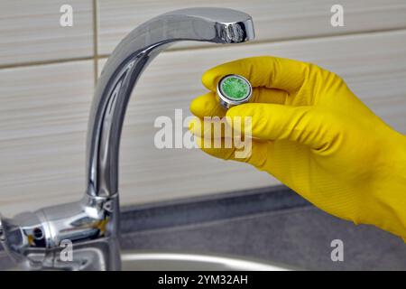 person in yellow rubber gloves changing clogged faucet aerator Stock Photo