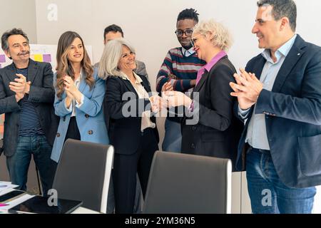 Diverse business professionals celebrating successful deal with handshake while team applauding in modern office Stock Photo