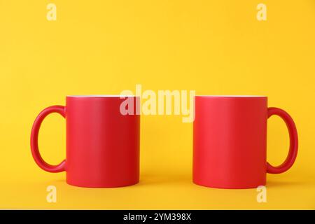 Two blank red mugs on yellow background. Mockup for design Stock Photo