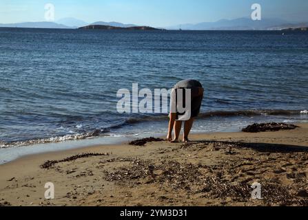 Woman collecting sea glass and shells on Vouliagmeni Beach Attica Athens Greece Stock Photo