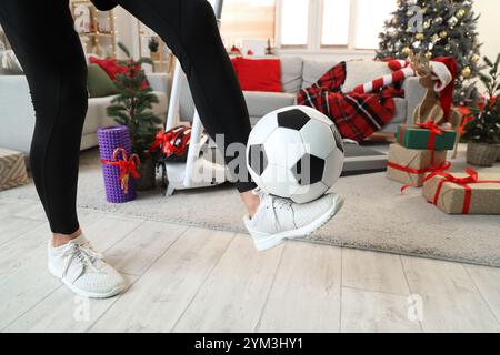Young sporty man playing with new soccer ball at home decorated for Christmas, closeup Stock Photo