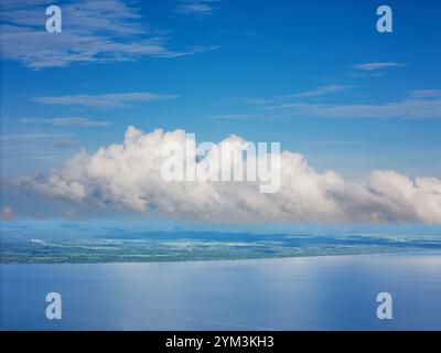 Fluffy white clouds float over serene ocean, reflecting  clear blue sky during peaceful day. Stock Photo