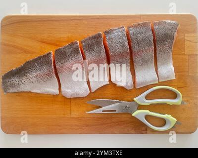 Cut raw Sea Trout fish fillet and scissors on wooden cutting board Stock Photo