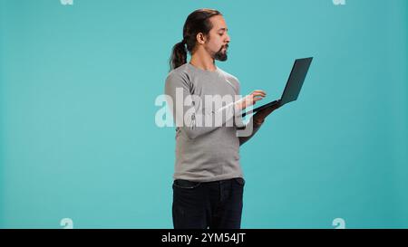 Portrait of smiling person spending time on laptop, isolated over studio background. Cheerful man checking social media posts on notebook, enjoying leisure time, camera A Stock Photo